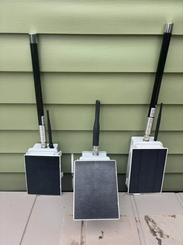Three completed Sid-NY solder-free solar repeater units showing white IP65 enclosures with 5 dBi omni antennas and integrated solar panels